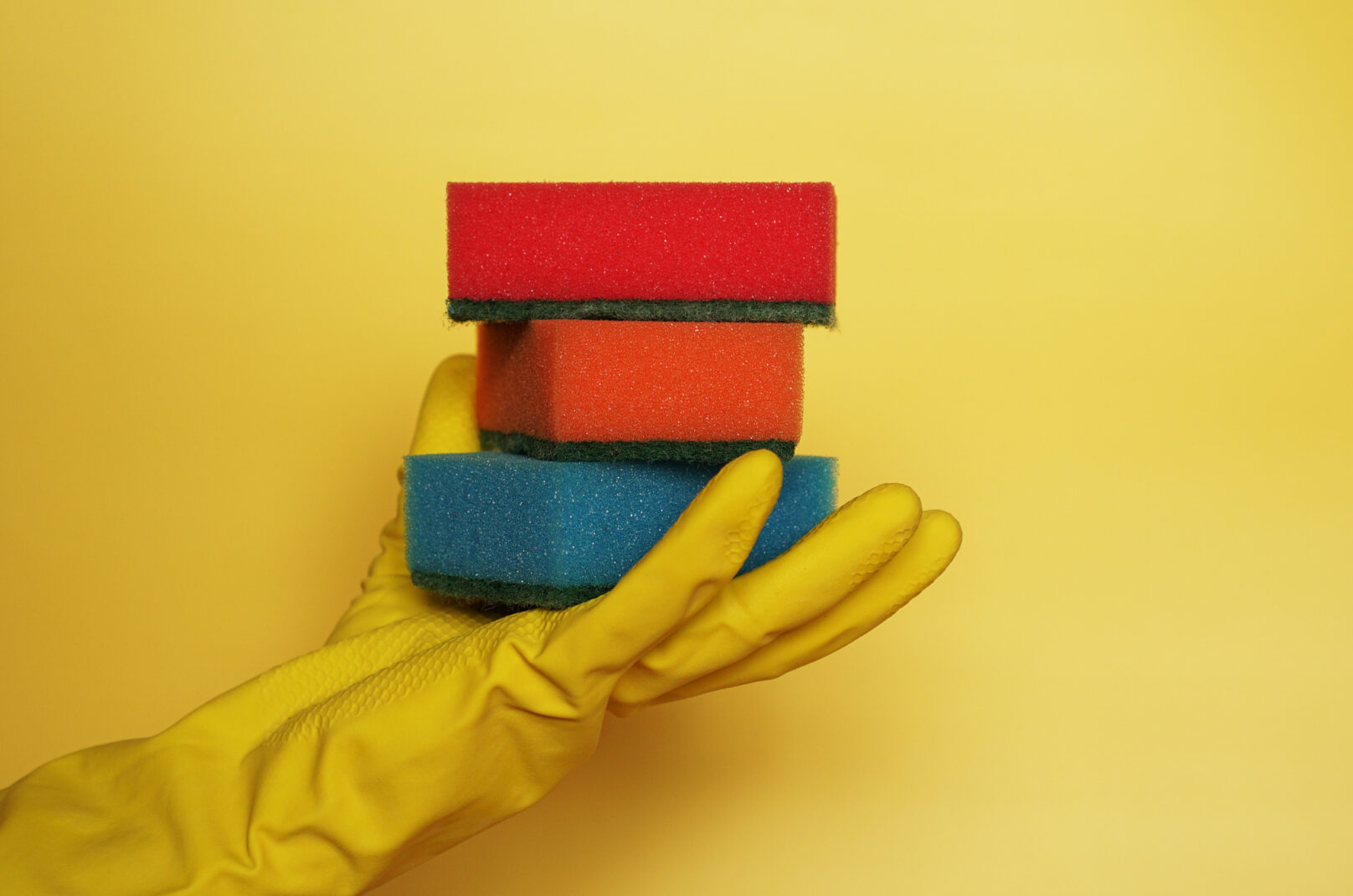 Hand in glove holding few washing sponges on yellow background - amount of housework concept